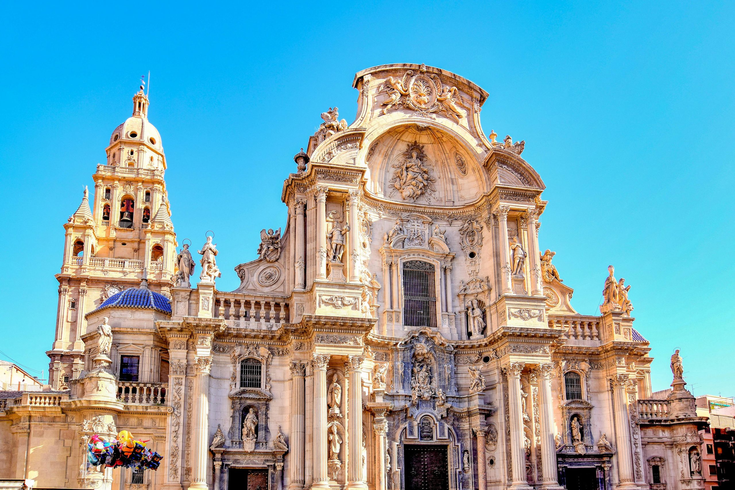 Intricate Baroque architecture of the Cathedral of Murcia against a clear blue sky.